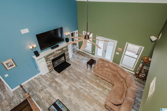 living room with a stone fireplace, a high ceiling, wood finished floors, and a ceiling fan