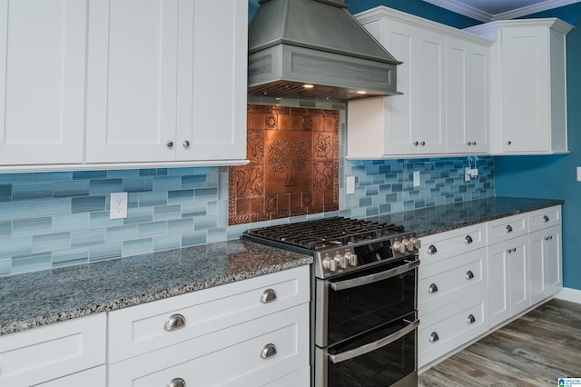 kitchen with range with two ovens, custom exhaust hood, dark stone countertops, and white cabinetry