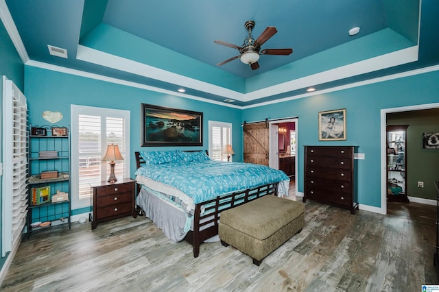 bedroom with wood finished floors, baseboards, visible vents, a tray ceiling, and a barn door