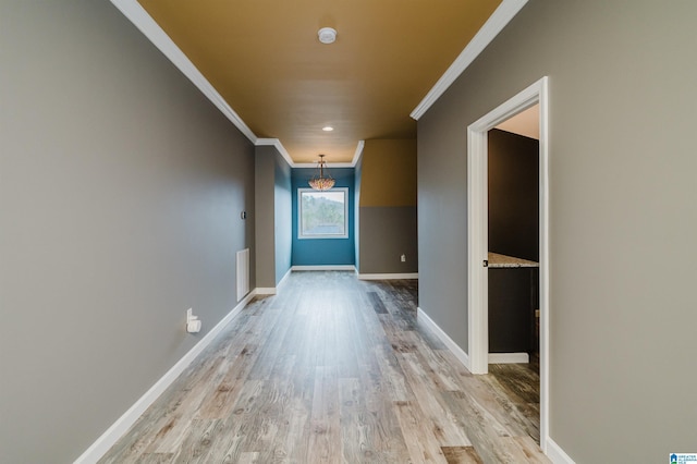 hallway featuring visible vents, baseboards, light wood-style floors, and crown molding