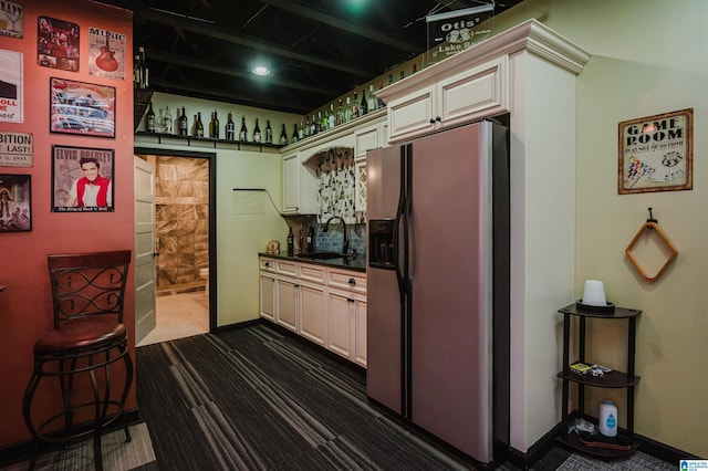 kitchen with baseboards, a sink, dark countertops, cream cabinets, and stainless steel fridge