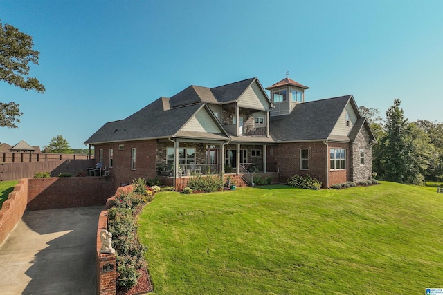 back of house featuring brick siding, fence, covered porch, a yard, and a balcony