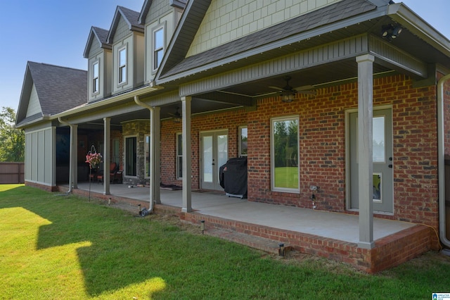 back of property with a yard, roof with shingles, brick siding, ceiling fan, and a patio area