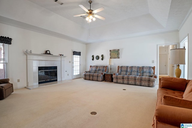 carpeted living area with a tray ceiling, visible vents, a fireplace, and a ceiling fan