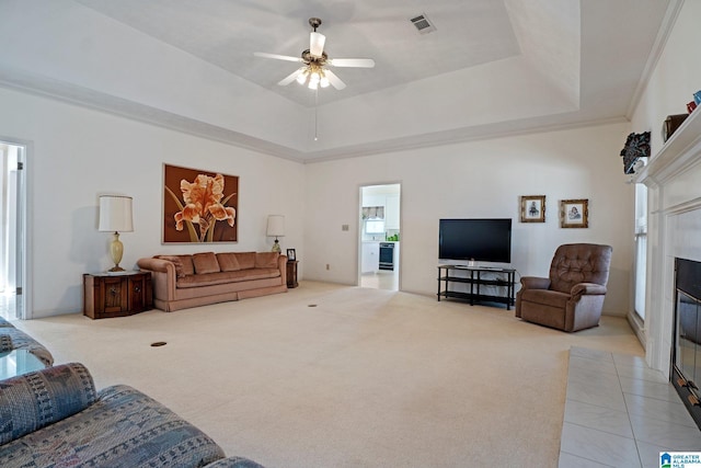 living area featuring a ceiling fan, a raised ceiling, light colored carpet, and a tile fireplace