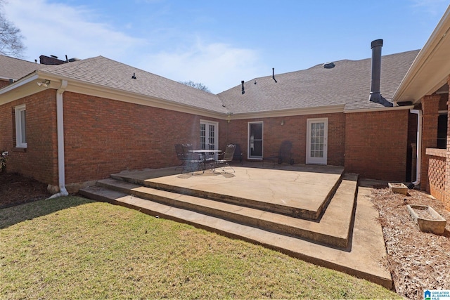 back of property featuring brick siding, a patio area, a shingled roof, and a lawn