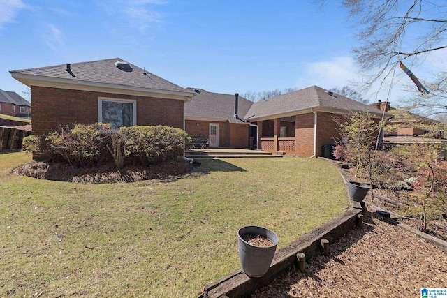 rear view of property featuring a yard, brick siding, and a shingled roof