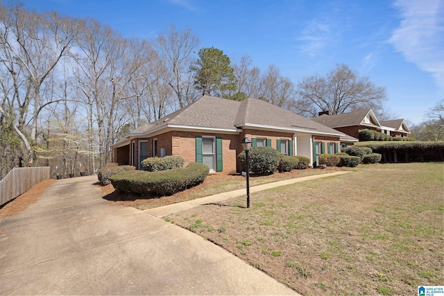 ranch-style home featuring a front yard, fence, driveway, roof with shingles, and brick siding