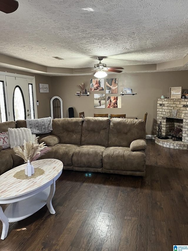 living room featuring ceiling fan, dark wood-type flooring, a fireplace, and a textured ceiling