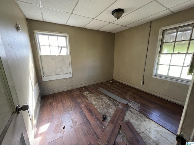 empty room with a healthy amount of sunlight, a paneled ceiling, and hardwood / wood-style flooring