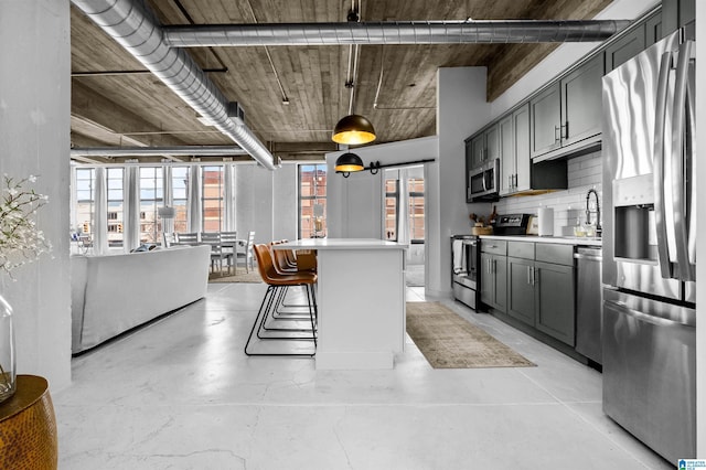 kitchen with a kitchen bar, a kitchen island, stainless steel appliances, decorative backsplash, and concrete flooring