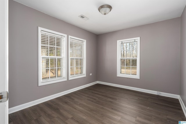 spare room featuring visible vents, baseboards, and dark wood-style flooring