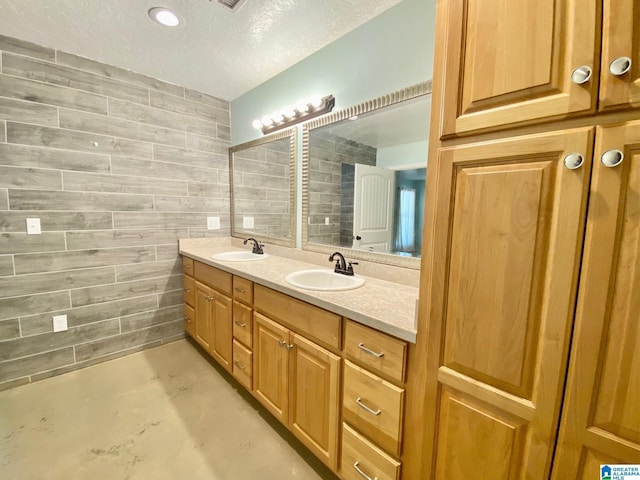 bathroom with a textured ceiling, double vanity, concrete floors, and a sink