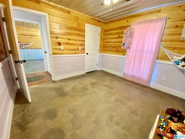 unfurnished bedroom with wooden walls, a ceiling fan, and concrete floors