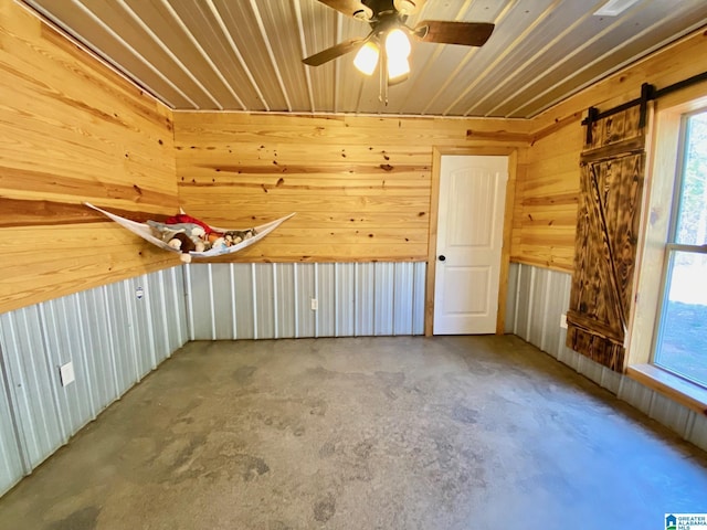 bonus room with a wealth of natural light, wooden walls, concrete floors, and ceiling fan