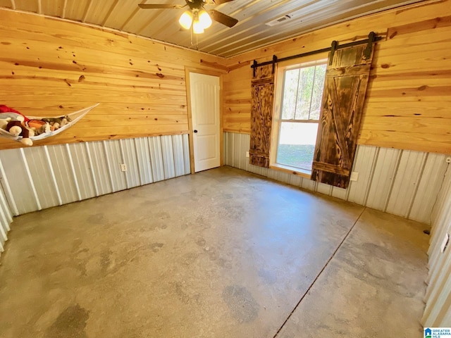 interior space with visible vents, wooden walls, concrete flooring, and a ceiling fan