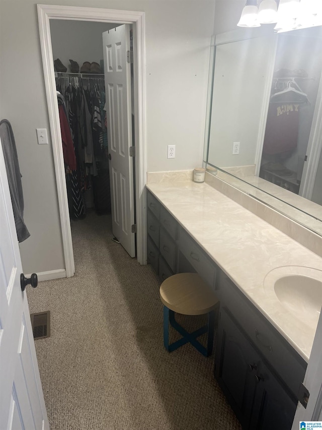 bathroom with visible vents, carpet, a walk in closet, and vanity