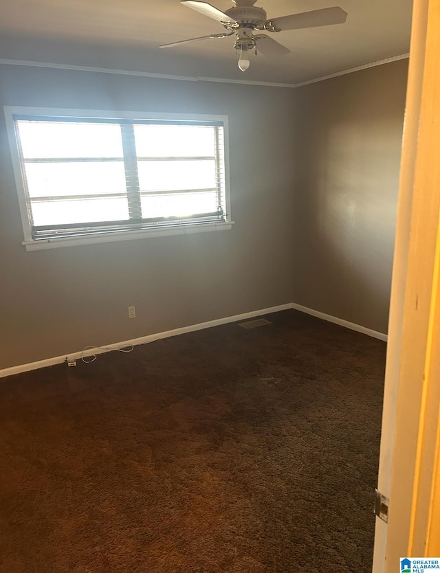 empty room featuring visible vents, ornamental molding, a ceiling fan, dark carpet, and baseboards