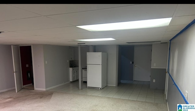 finished below grade area featuring light tile patterned floors, light colored carpet, freestanding refrigerator, and a paneled ceiling