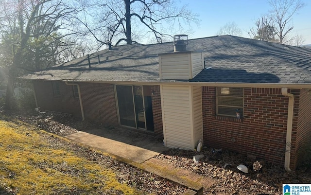 back of house featuring brick siding and a shingled roof