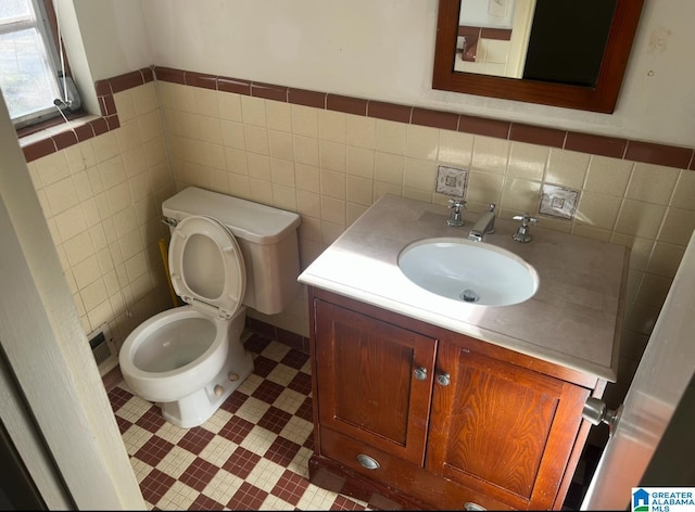 half bathroom featuring tile patterned flooring, toilet, vanity, and tile walls