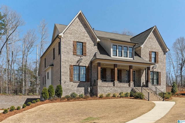 view of front of property with board and batten siding, brick siding, a porch, and roof with shingles