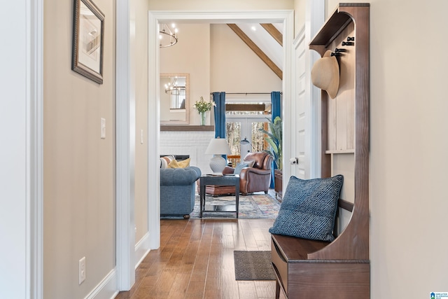 hallway with baseboards, beamed ceiling, an inviting chandelier, high vaulted ceiling, and wood-type flooring