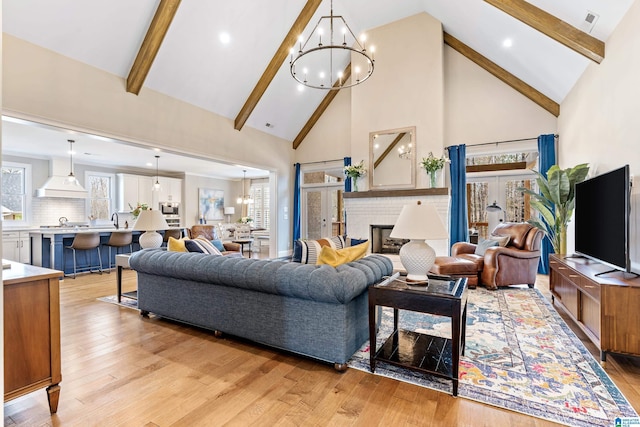 living room featuring light wood finished floors, a brick fireplace, a chandelier, beam ceiling, and high vaulted ceiling