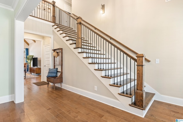 staircase with hardwood / wood-style floors, baseboards, a towering ceiling, and ornamental molding