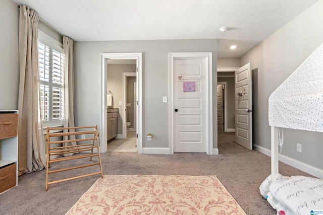 carpeted bedroom featuring ensuite bath and baseboards