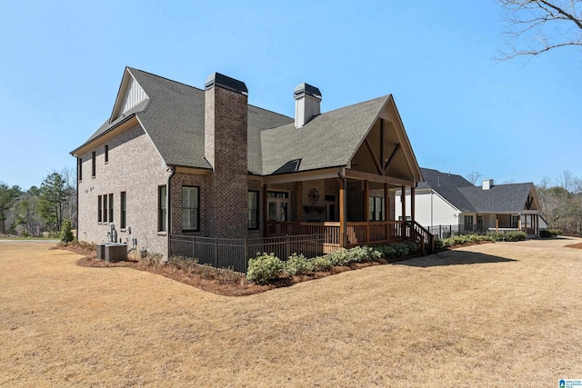 back of property featuring a porch, a yard, brick siding, central AC unit, and a chimney