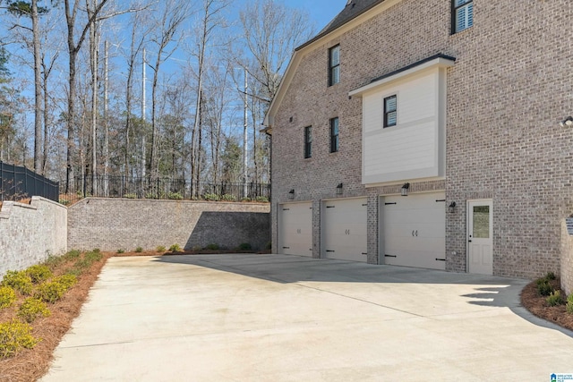 view of side of home featuring brick siding, an attached garage, concrete driveway, and fence