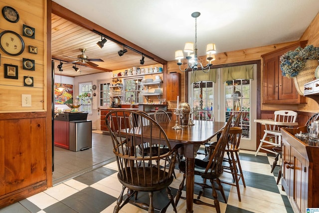 dining room featuring rail lighting, ceiling fan with notable chandelier, and wood walls