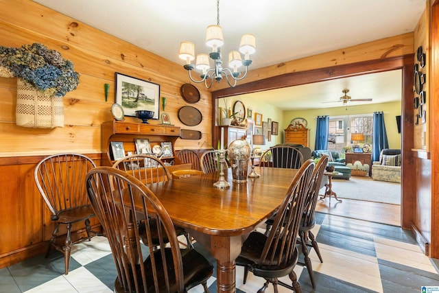 dining room with wood finished floors, wood walls, and ceiling fan with notable chandelier