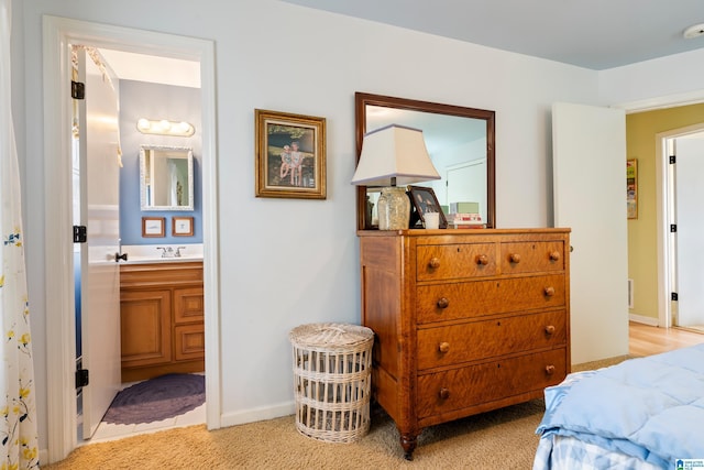 bedroom featuring connected bathroom, light colored carpet, baseboards, and a sink