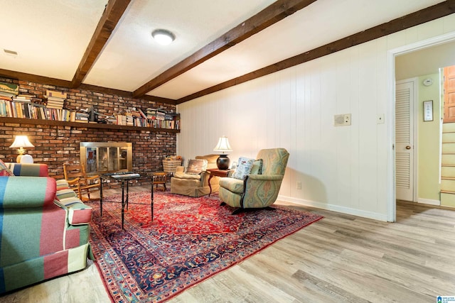 living area with a fireplace, beamed ceiling, wood finished floors, and baseboards