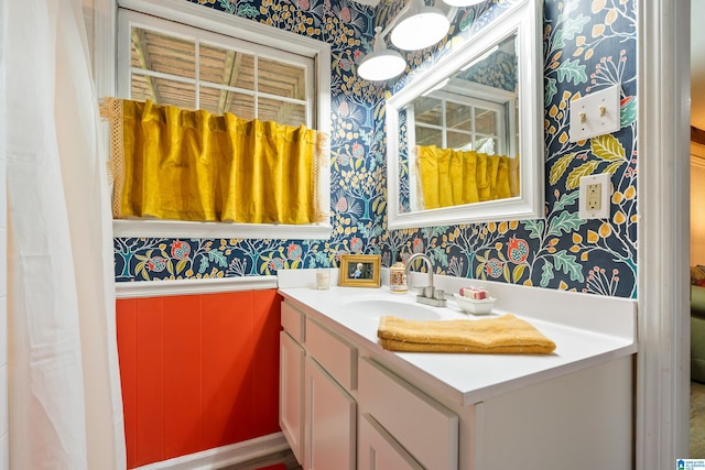 bathroom with wallpapered walls, vanity, and a wainscoted wall