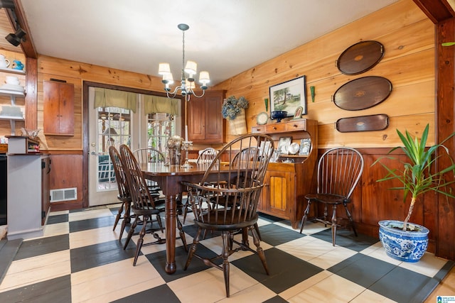 dining space with tile patterned floors, wooden walls, visible vents, and a chandelier