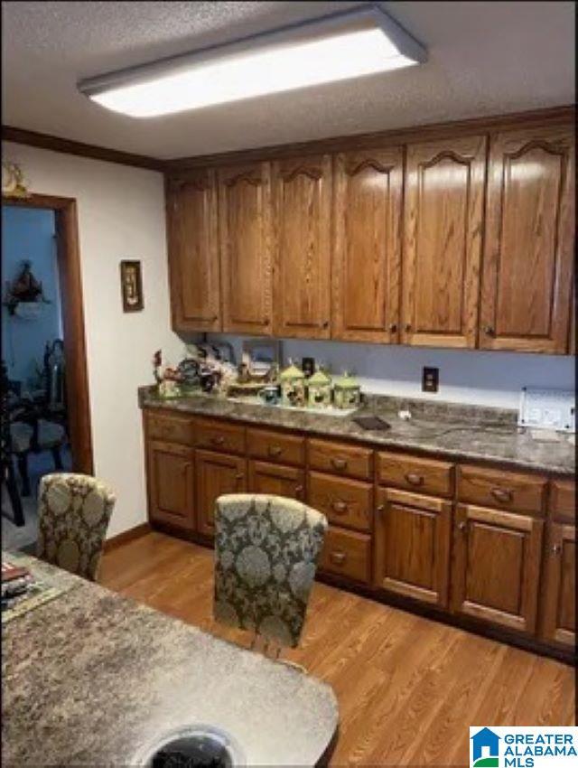 kitchen featuring light wood finished floors, brown cabinets, a textured ceiling, and ornamental molding