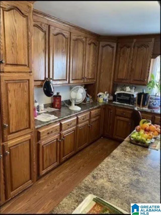 kitchen featuring light stone counters, a toaster, wood finished floors, and brown cabinets