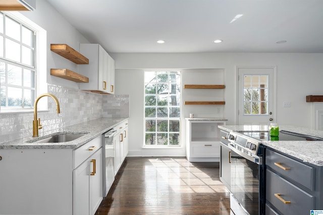 kitchen featuring open shelves, light stone counters, decorative backsplash, appliances with stainless steel finishes, and a sink