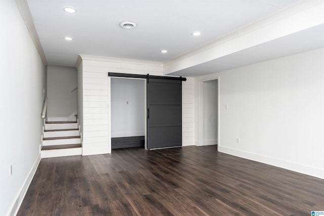 unfurnished bedroom featuring a barn door, baseboards, a closet, and dark wood-style flooring