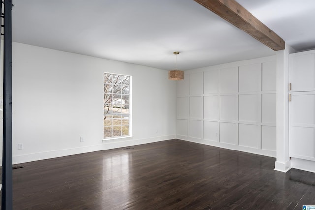 empty room featuring a decorative wall, dark wood-style floors, beamed ceiling, and baseboards