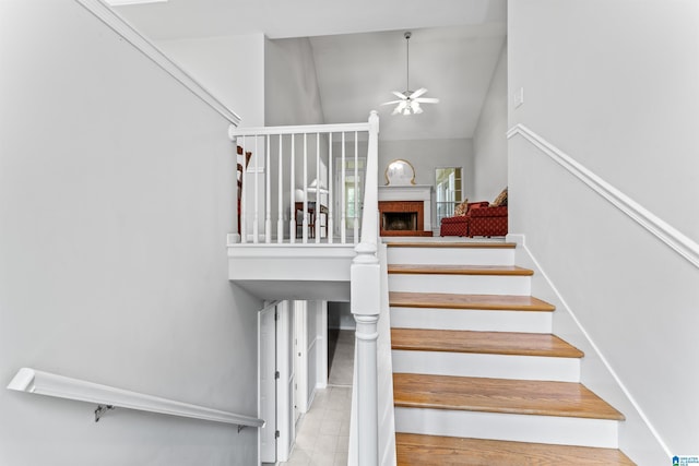 staircase with high vaulted ceiling, a ceiling fan, and a fireplace