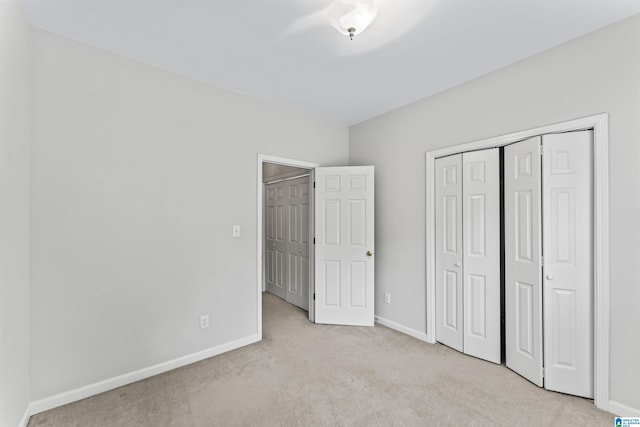 unfurnished bedroom with light carpet, a closet, and baseboards