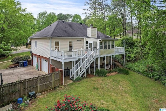 rear view of house featuring stairway, concrete driveway, a wooden deck, a chimney, and a yard