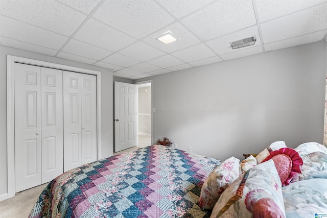 bedroom with a paneled ceiling, visible vents, light carpet, and a closet