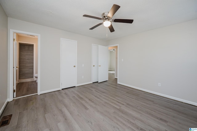 unfurnished bedroom with visible vents, ensuite bath, baseboards, and wood finished floors