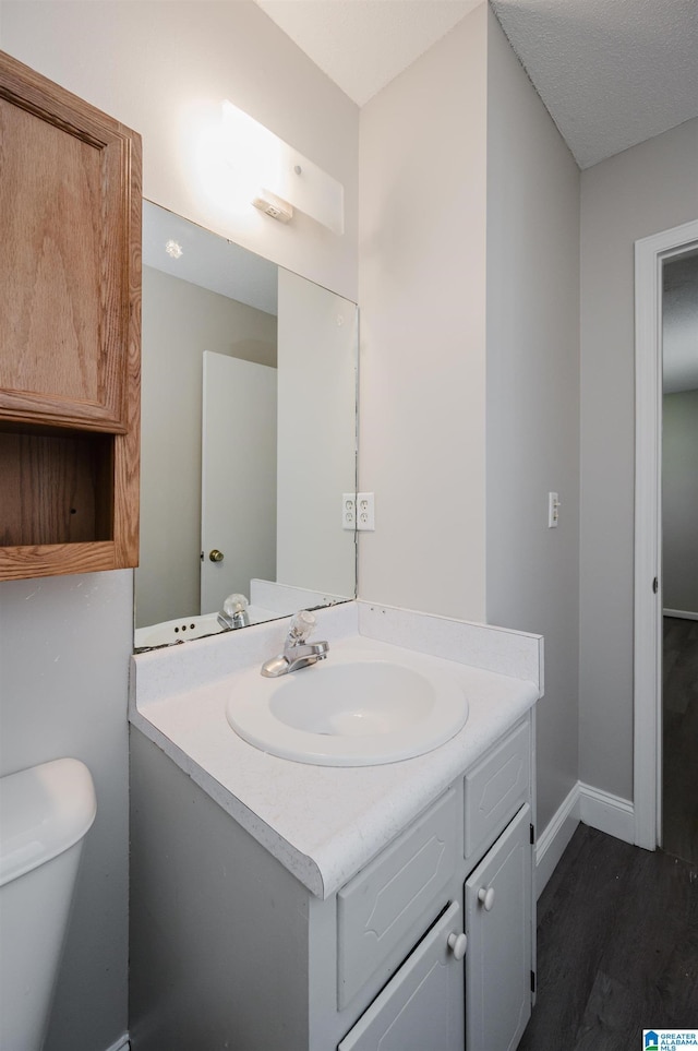 half bathroom with vanity, toilet, wood finished floors, and baseboards