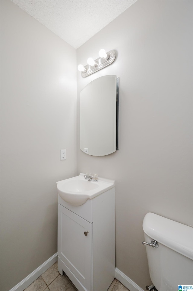 half bathroom with vanity, baseboards, a textured ceiling, tile patterned floors, and toilet